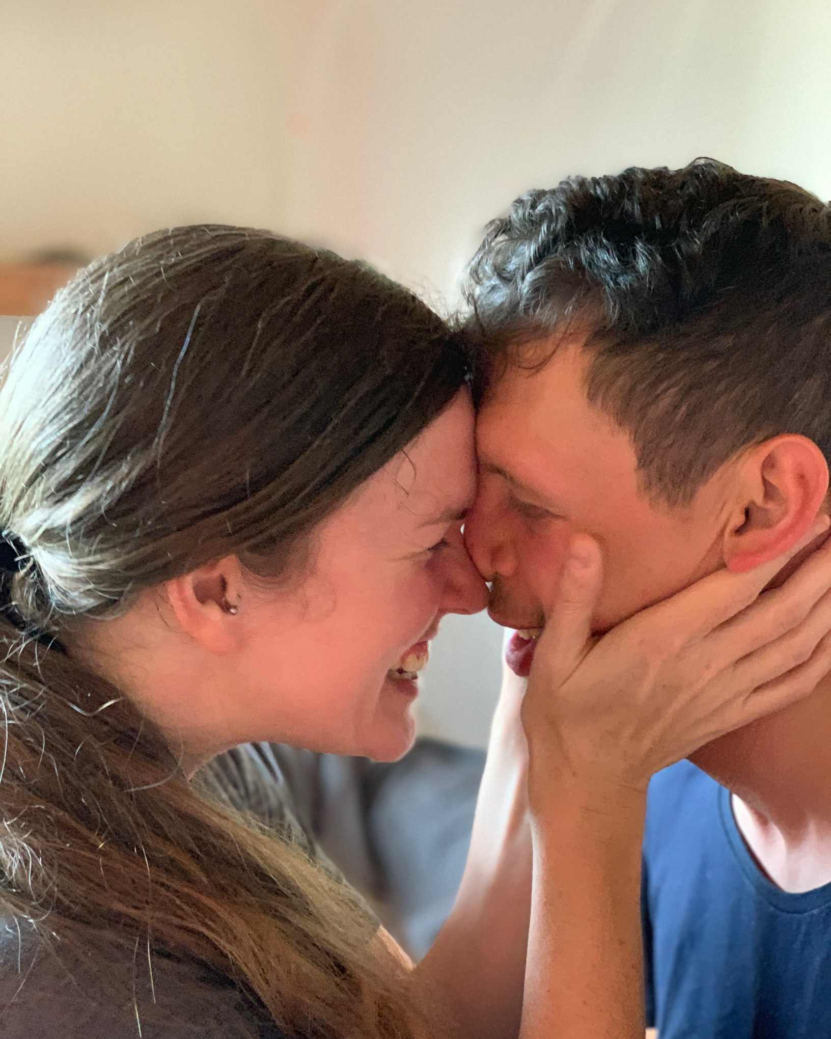 A young lady embraces a special needs young man, smiling and standing nose to nose.