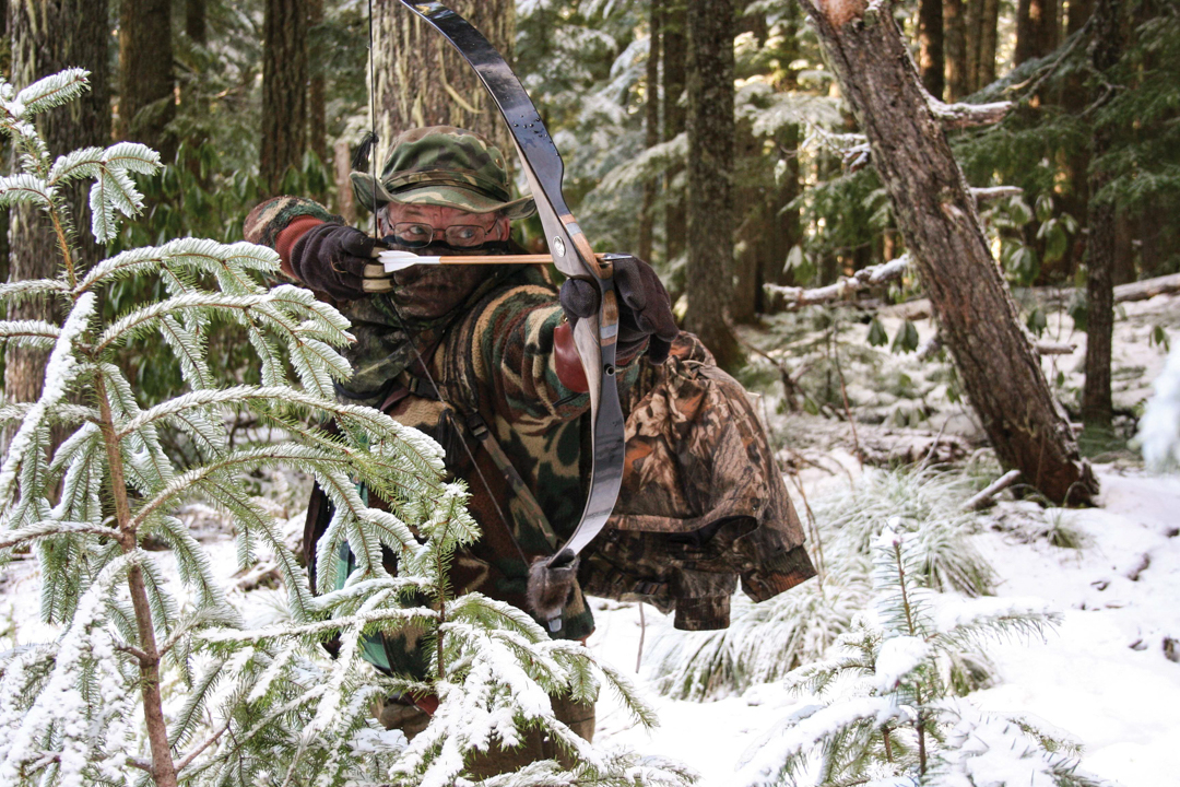 traditional bowhunter ready to shoot in snowy woods